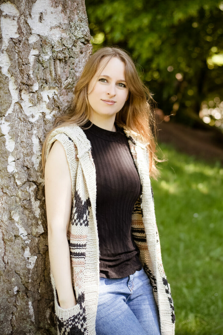 Webdesignerin Stefanie Schmiedeberg steht mit offenen blonden Haaren in der Natur an Baum angelehnt