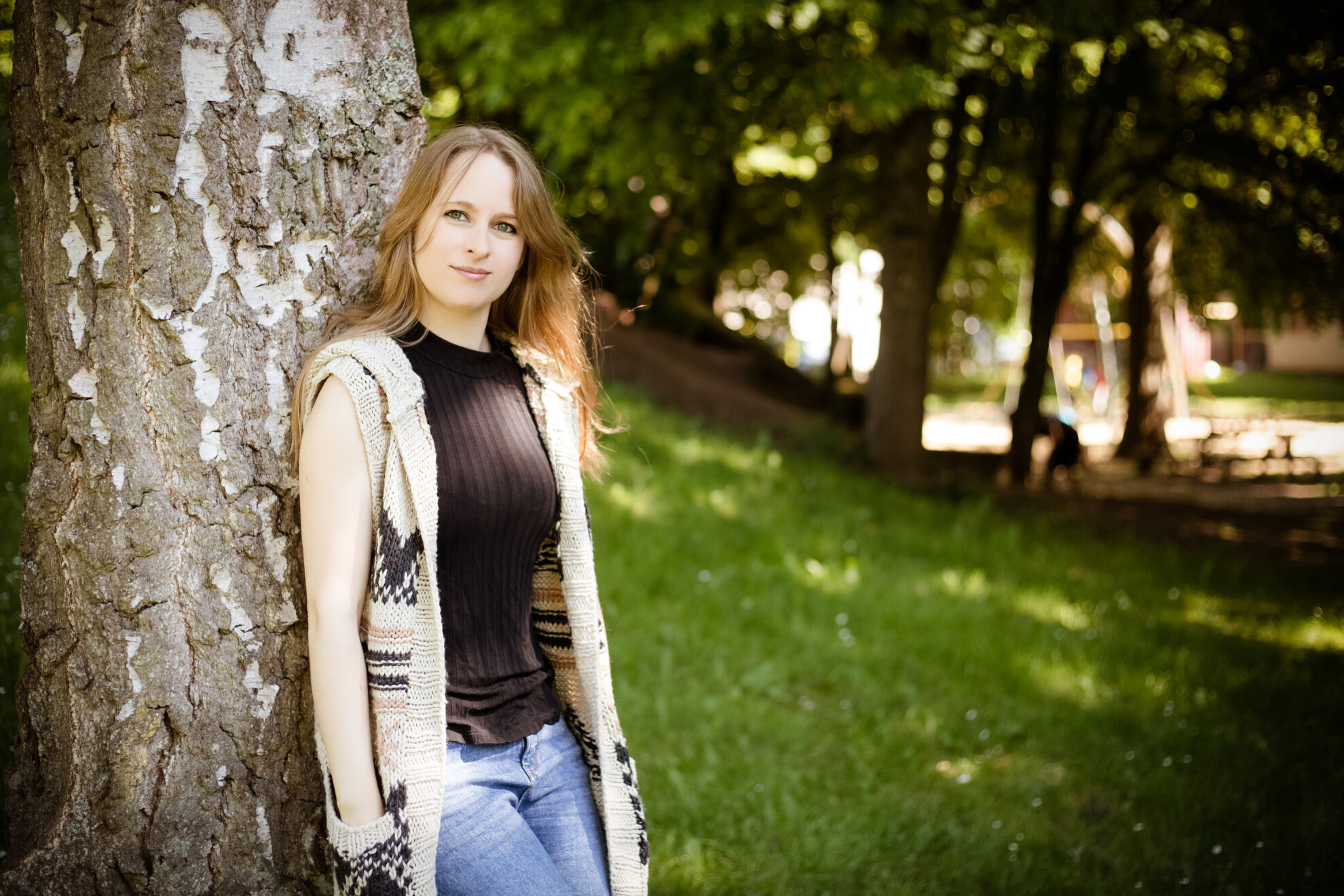 Stefanie Schmiedeberg steht in einem Park an einen Baum angelehnt.